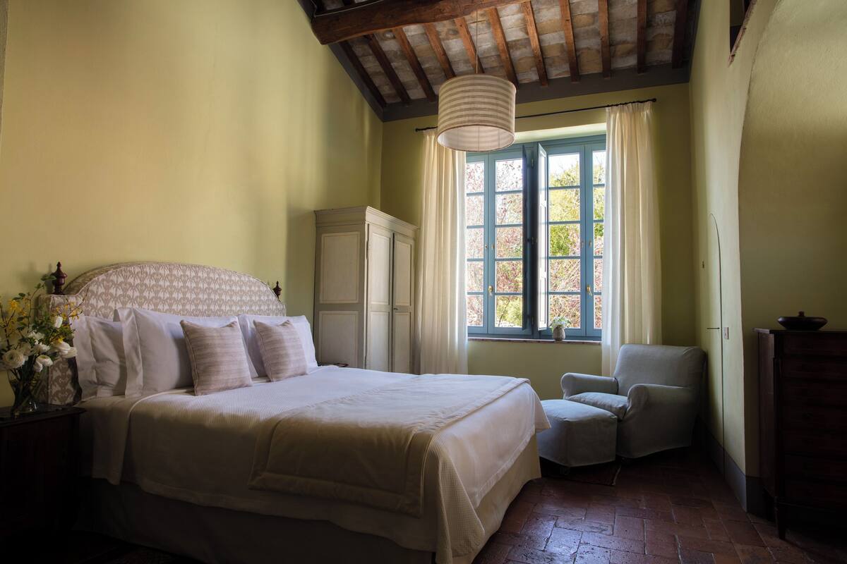 Un dormitorio con una cama grande, una silla, un armario y una ventana con cortinas.