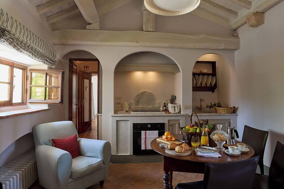 Un comedor con una mesa preparada para el desayuno, una chimenea y una cocina al fondo.