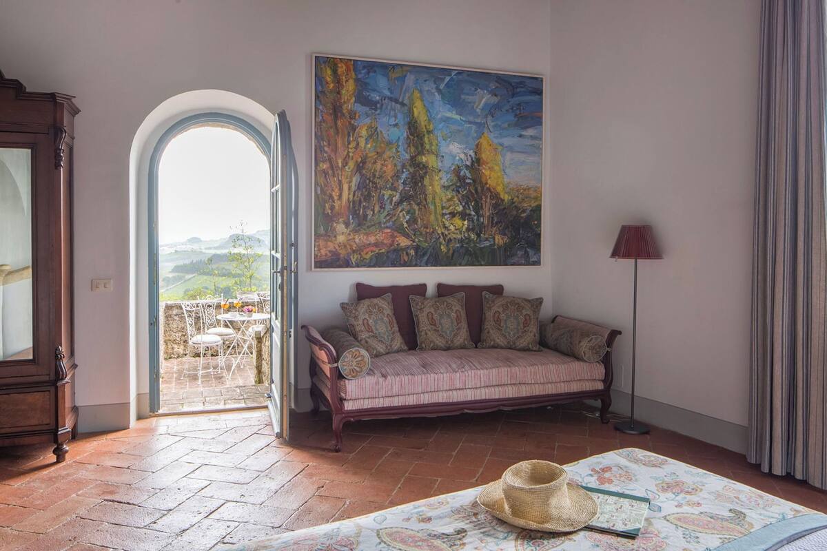 Una sala de estar con sofá, un cuadro, una lámpara y vistas a través de un ventanal.