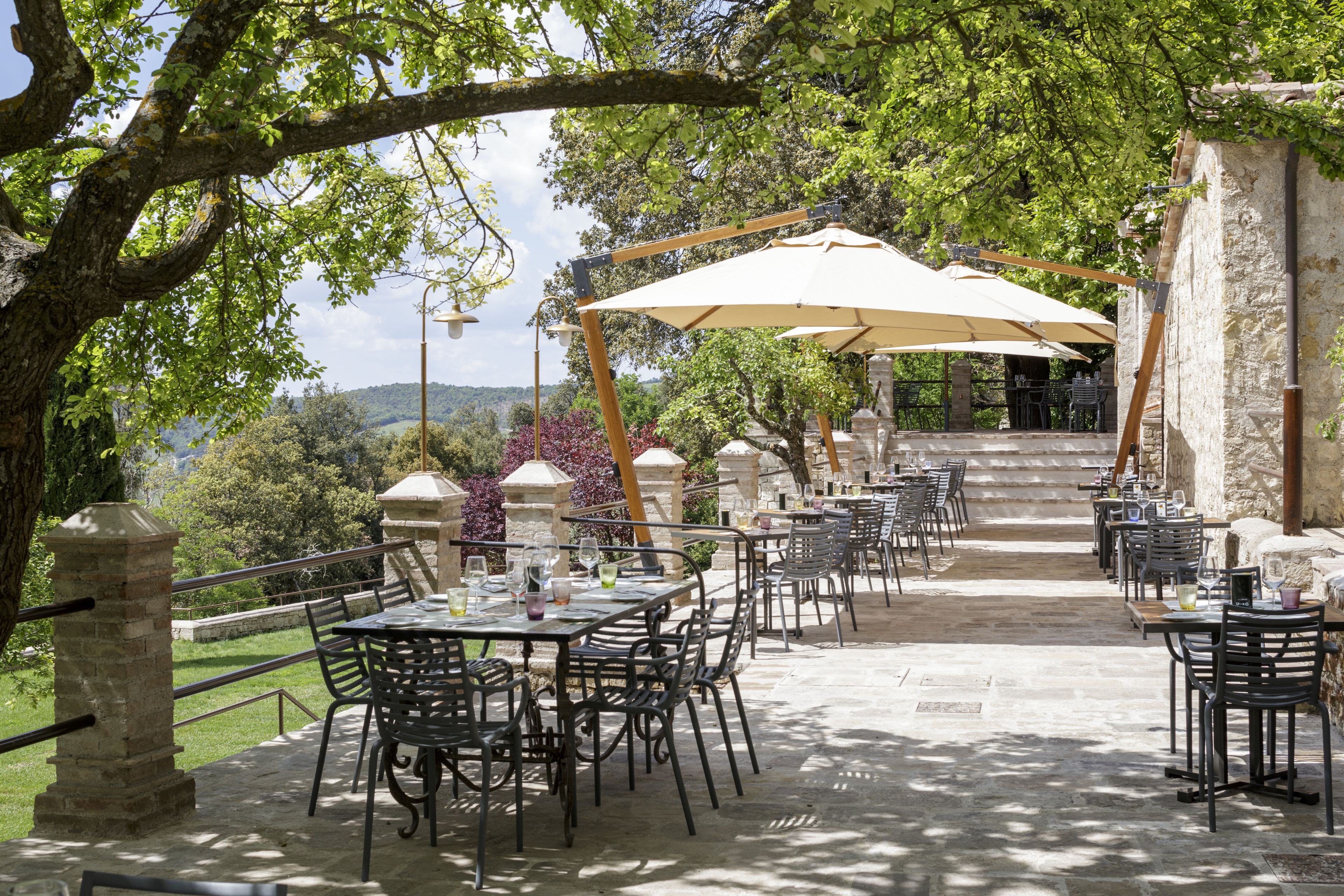Un patio al aire libre con mesas y sillas de piedra, una pérgola con toldo y vistas del paisaje circundante.