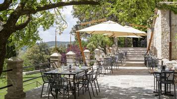 Un patio al aire libre con mesas y sillas de piedra, una pérgola con toldo y vistas del paisaje circundante.