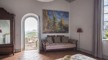 A room with a sofa, a painting, a table with a hat, and a view through an open door.