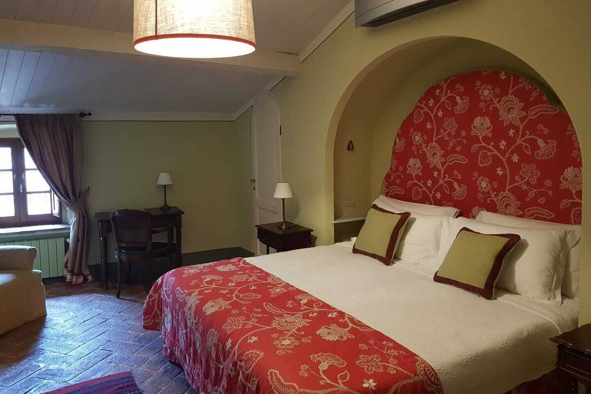Un dormitorio con una cama grande, un candelabro, un cabecero arqueado y un escritorio con una lámpara.