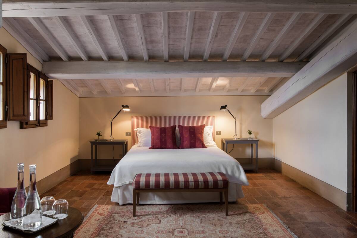 Un dormitorio con una cama grande, dos mesitas de noche, un banco y una alfombra estampada.