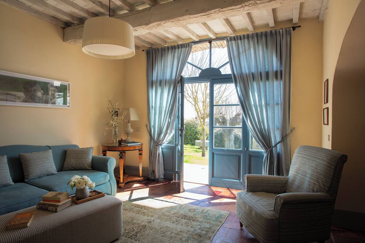 Una sala de estar acogedora con un sofá azul, un sillón a rayas y una mesa de centro de madera con libros y un jarrón.