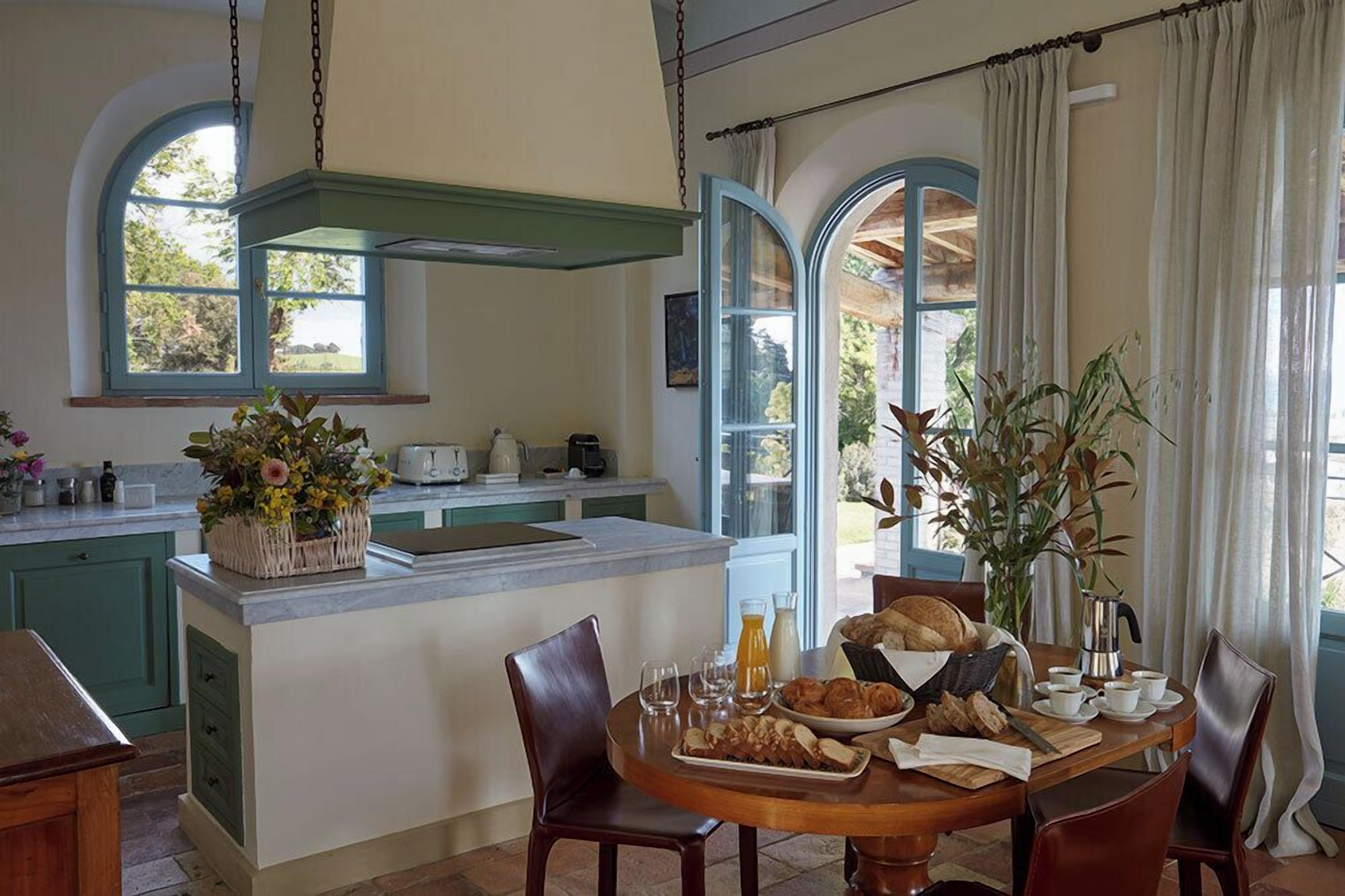 A kitchen with a central island, a dining table with chairs, and a view of the outdoors through large windows.