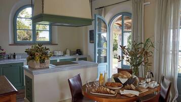 A kitchen with a central island, a dining table with chairs, and a view of the outdoors through large windows.
