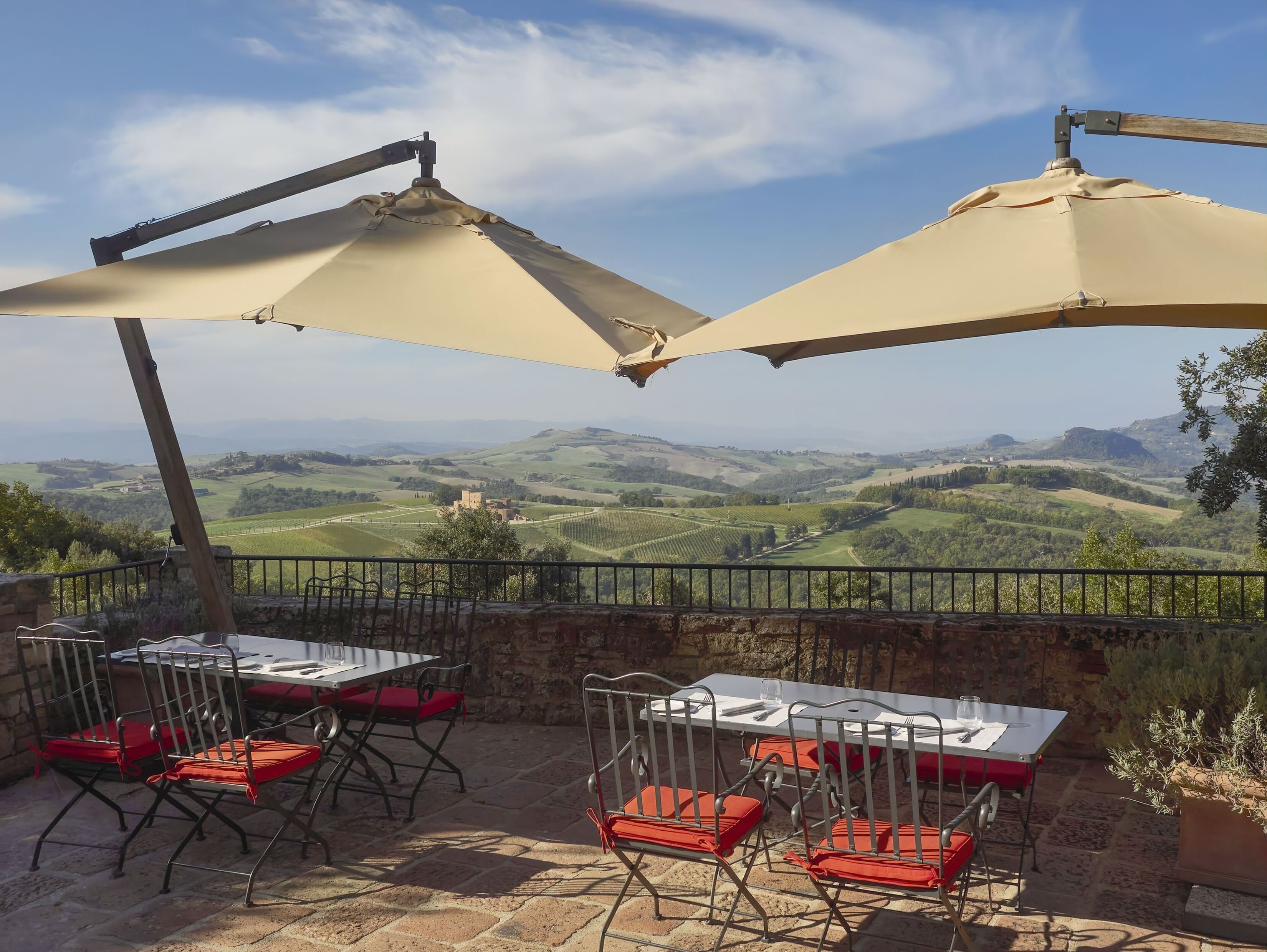A terrace with tables and chairs, a view of rolling hills, and a stone wall.