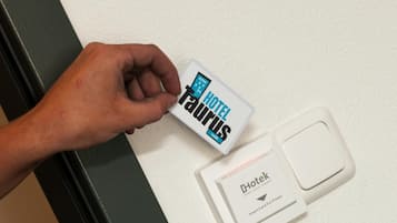 A hand inserting a hotel card into a card reader, with a card reader and a power outlet visible.