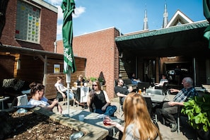 An outdoor seating area with tables and chairs, a green umbrella, and a brick building in the background. - Hotel Taurus (Cuijk)