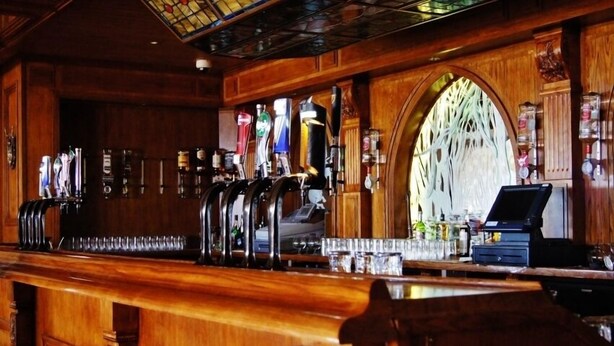 A bar area with multiple beer taps, a cash register, and a stained glass window. - The Hedges Hotel (Ballymoney)