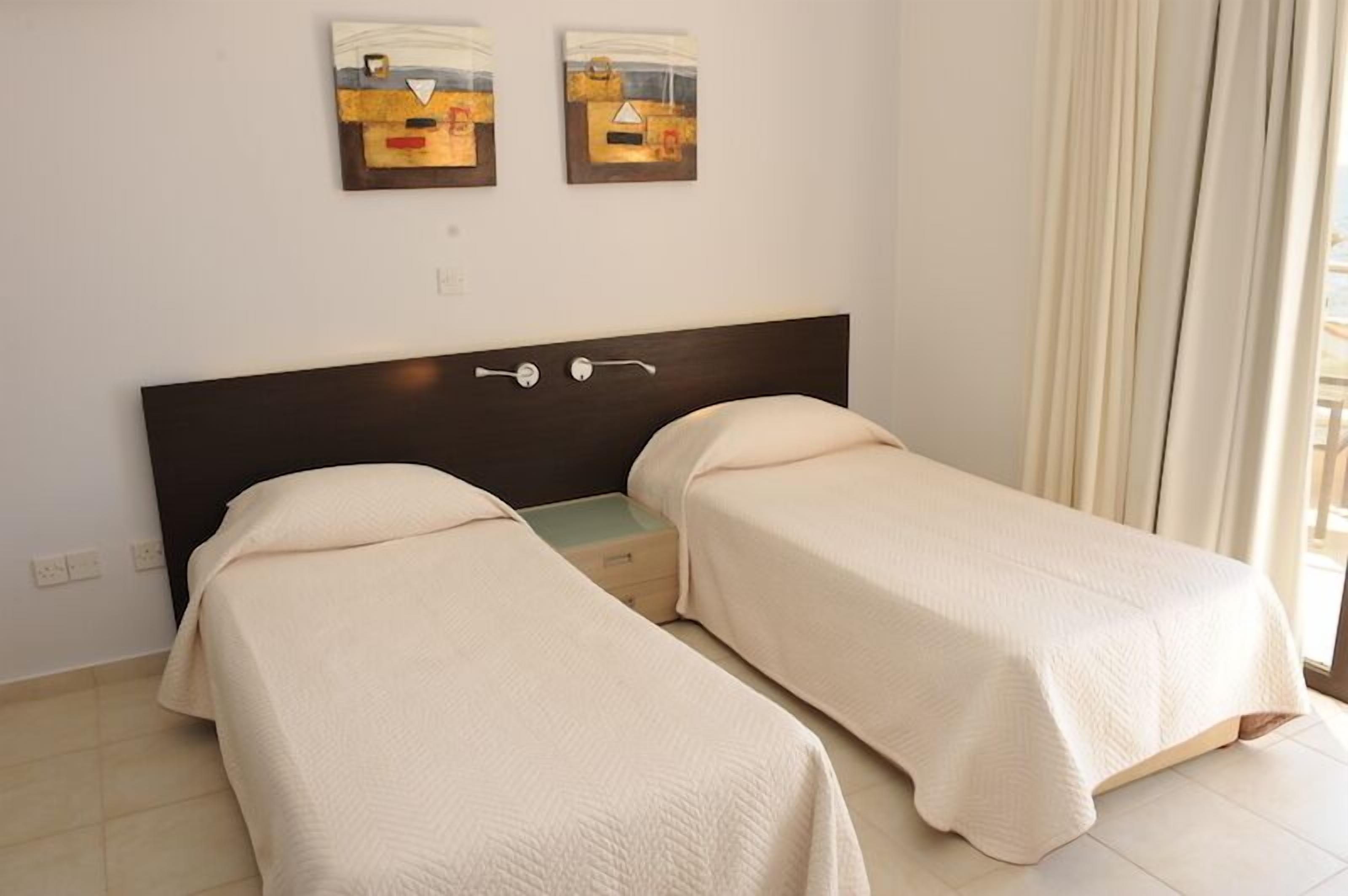 A room with two single beds, a dark headboard, and two abstract paintings on the wall.