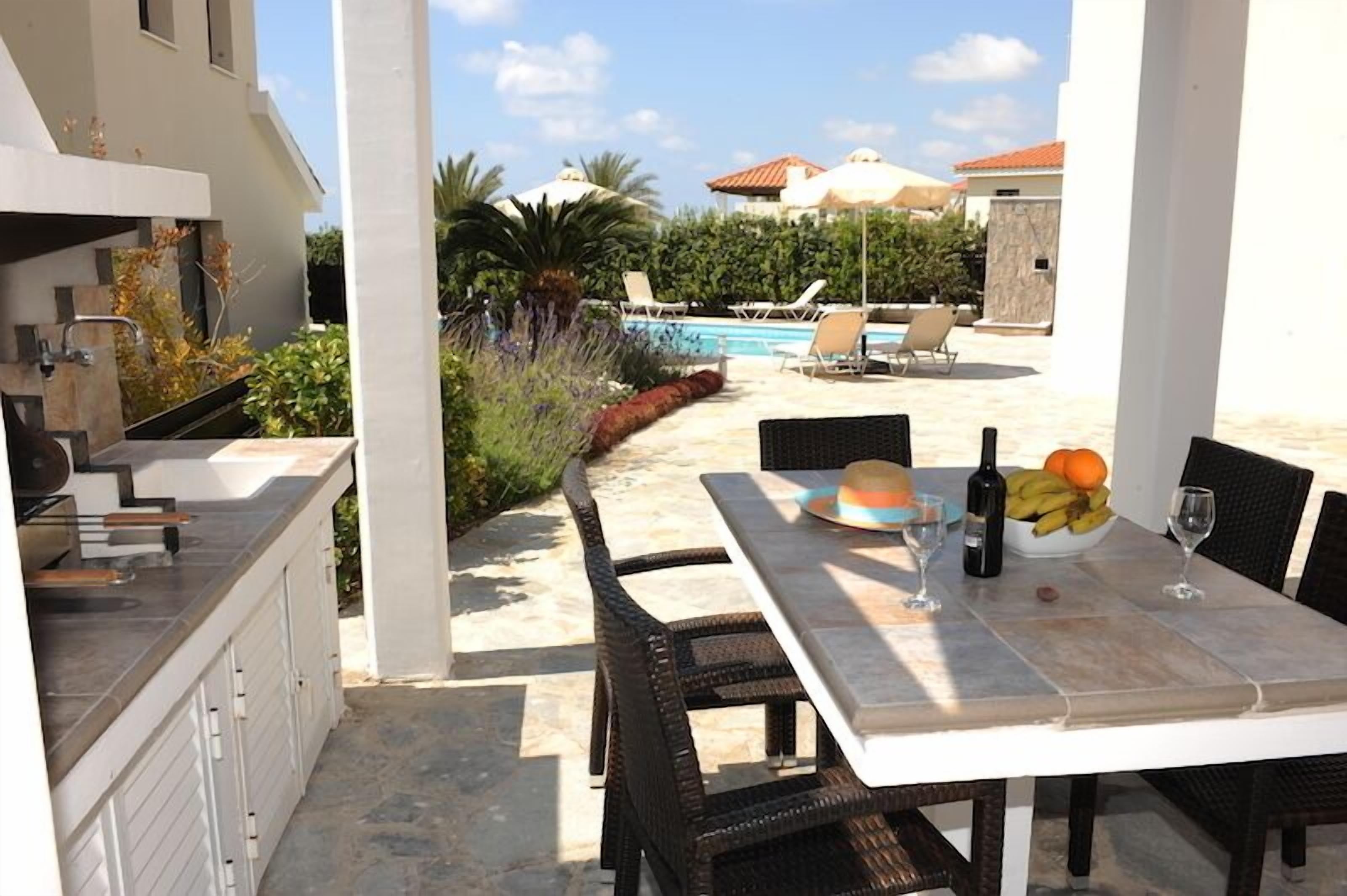An outdoor dining area with a table set for two, a bottle of wine, and a bowl of fruit.