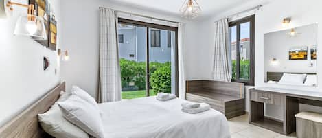 A modern hotel room with a bed, a desk, a mirror, and a view of greenery outside.