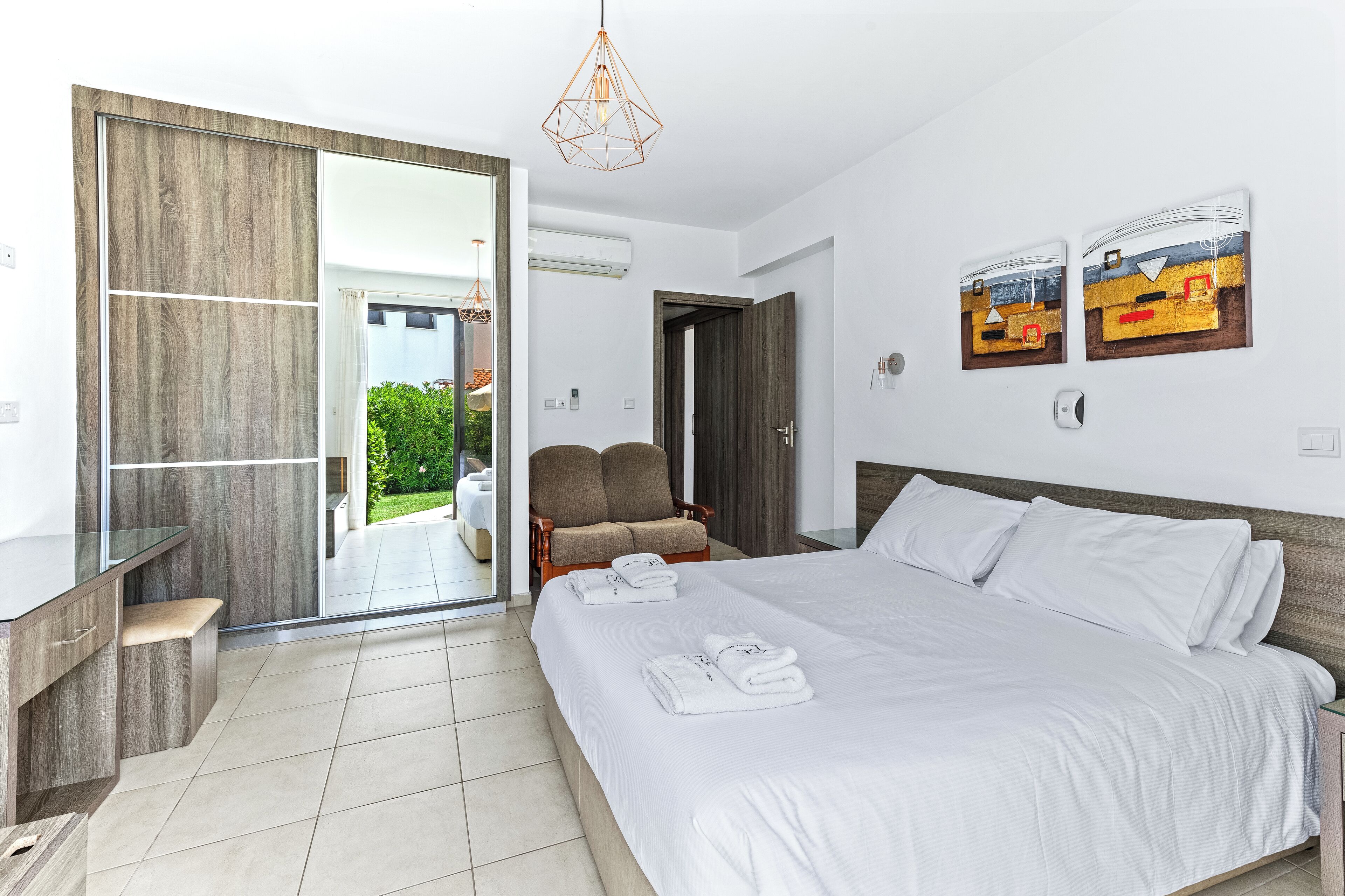 A modern hotel room with a large bed, a desk, a chair, and a sliding glass door leading to a balcony.