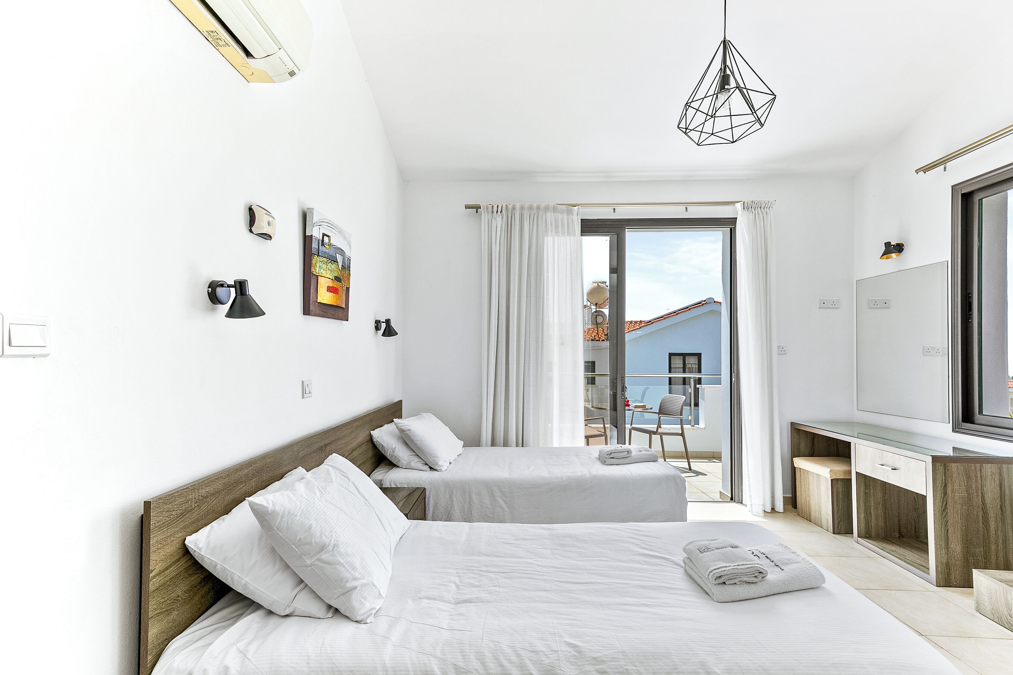 Une chambre d’hôtel moderne avec deux lits, un bureau et une grande fenêtre donnant sur un immeuble.