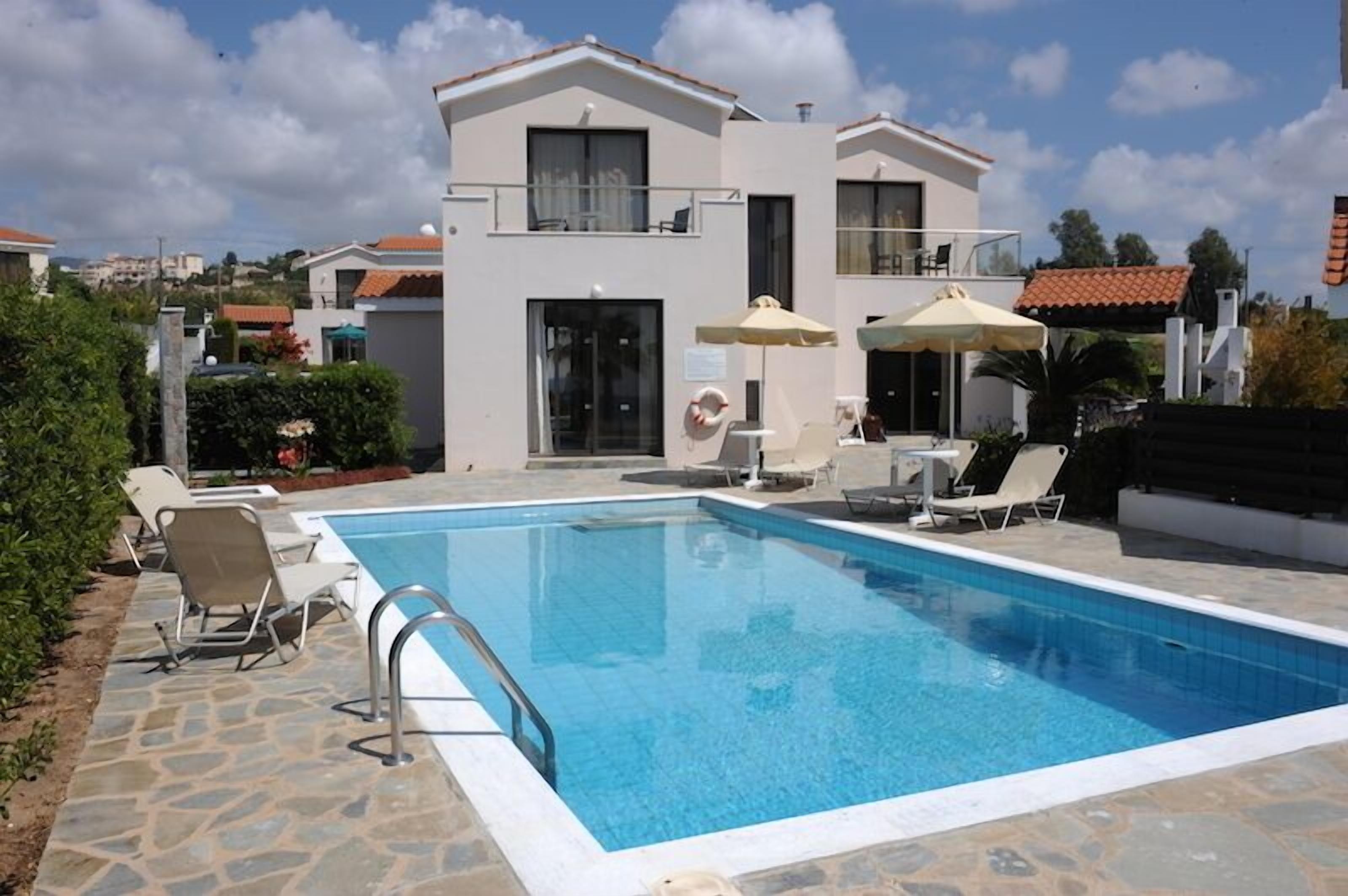A modern two-story building with a swimming pool, outdoor seating, and a clear sky.