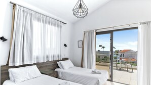 A hotel room with two beds, a balcony with a view, and a modern chandelier. - Platzia Beach Villas (Kissonerga)