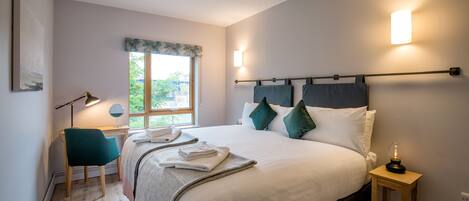 A neatly arranged bedroom with a large bed, bedside lamps, a desk, and a window with a view.