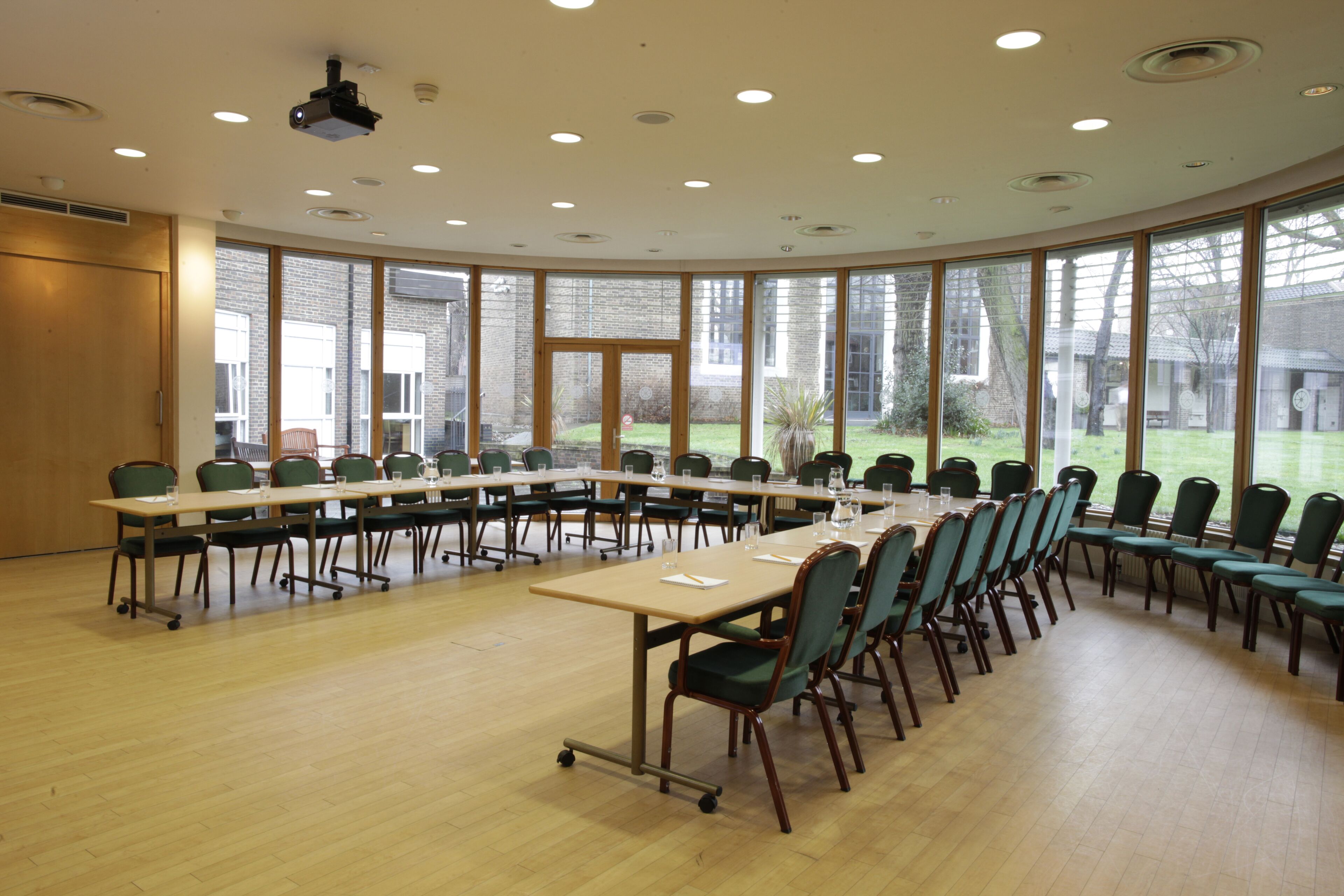 Un salón de conferencias con una larga mesa, sillas, ventanas amplias y un proyector.