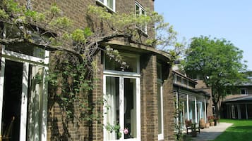 Traditional brick building with a corner entrance and large windows, set amidst a well-manicured lawn and shaded by a large tree.