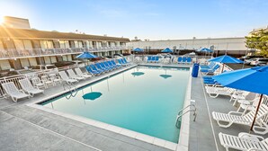 Una piscina amb gandules i para-sols, envoltada d'un edifici amb balcons.