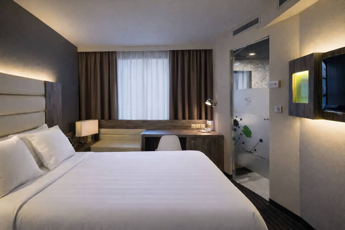 A hotel room with a large bed, a desk, a chair, a TV, and a window with curtains.