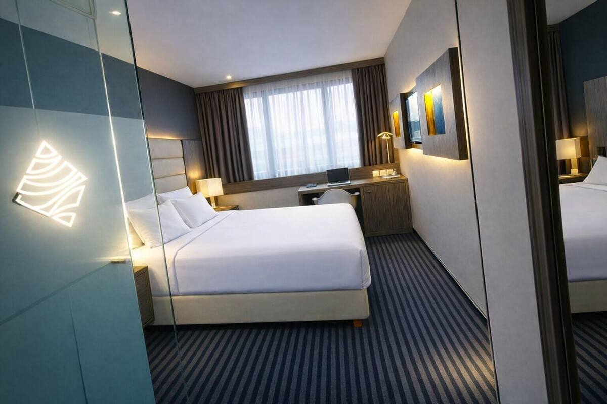 A modern hotel room with a large bed, a desk, a chair, a mirror, and a window with curtains.