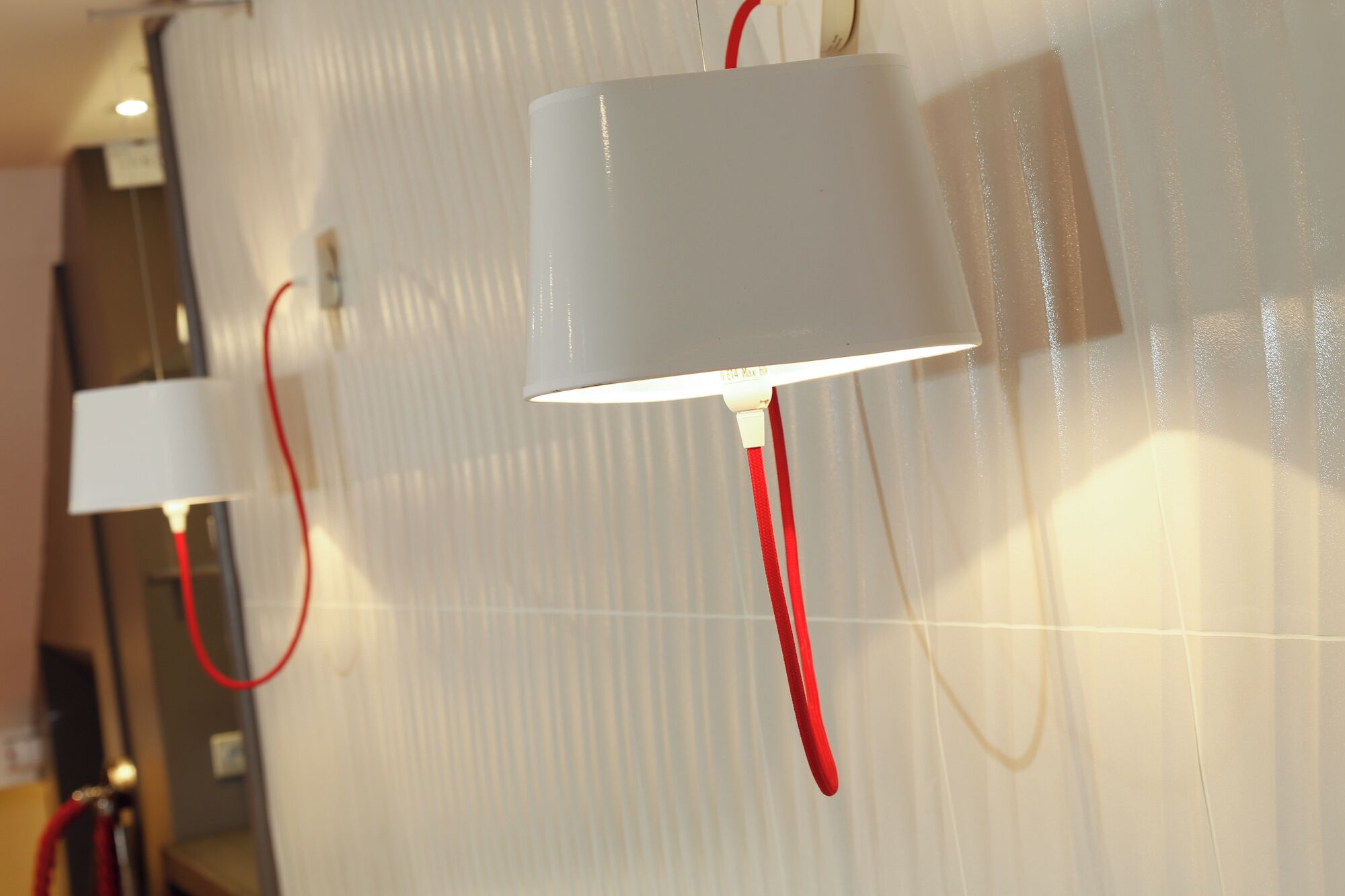 Des lampes murales dotées de câbles rouges, fixées sur un mur à texture.