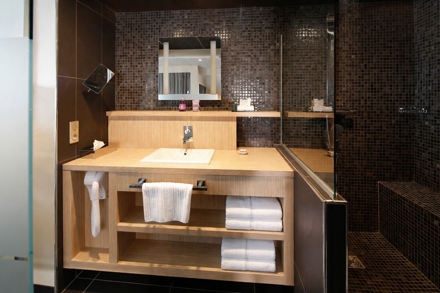 A modern bathroom with a wooden vanity, a mirror, and a glass shower enclosure.