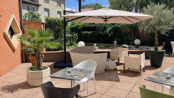 Un patio al aire libre con una mesa, sillas, un paraguas grande y plantas en macetas.