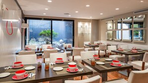 Un comedor moderno con mesas dispuestas para una ceremonia de té, vistas a un jardín a través de grandes ventanales y un diseño de interiores contemporáneo.