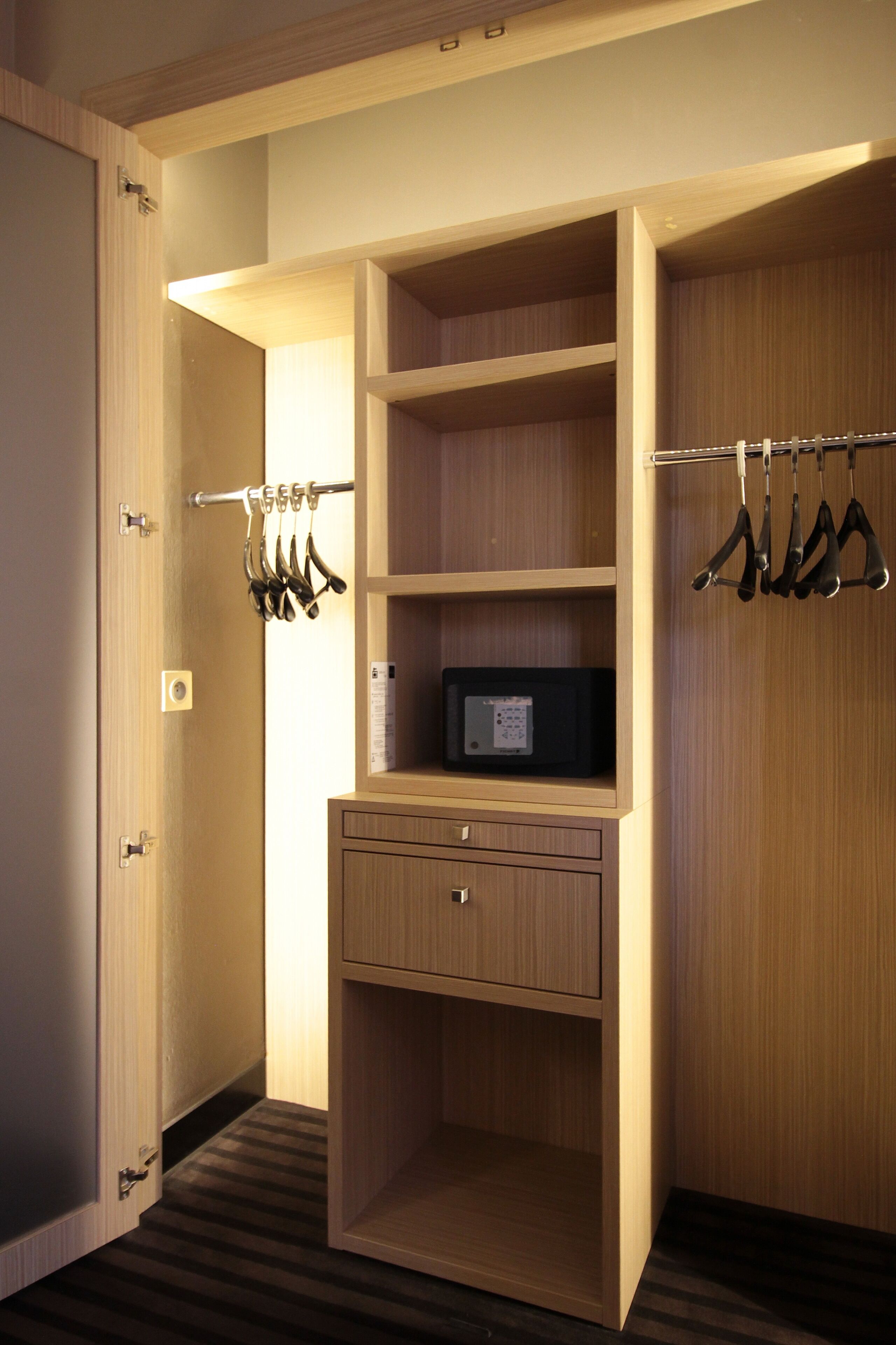 Een inloopkast met openslaande deuren, planken, een magnetron en hangende kleding.