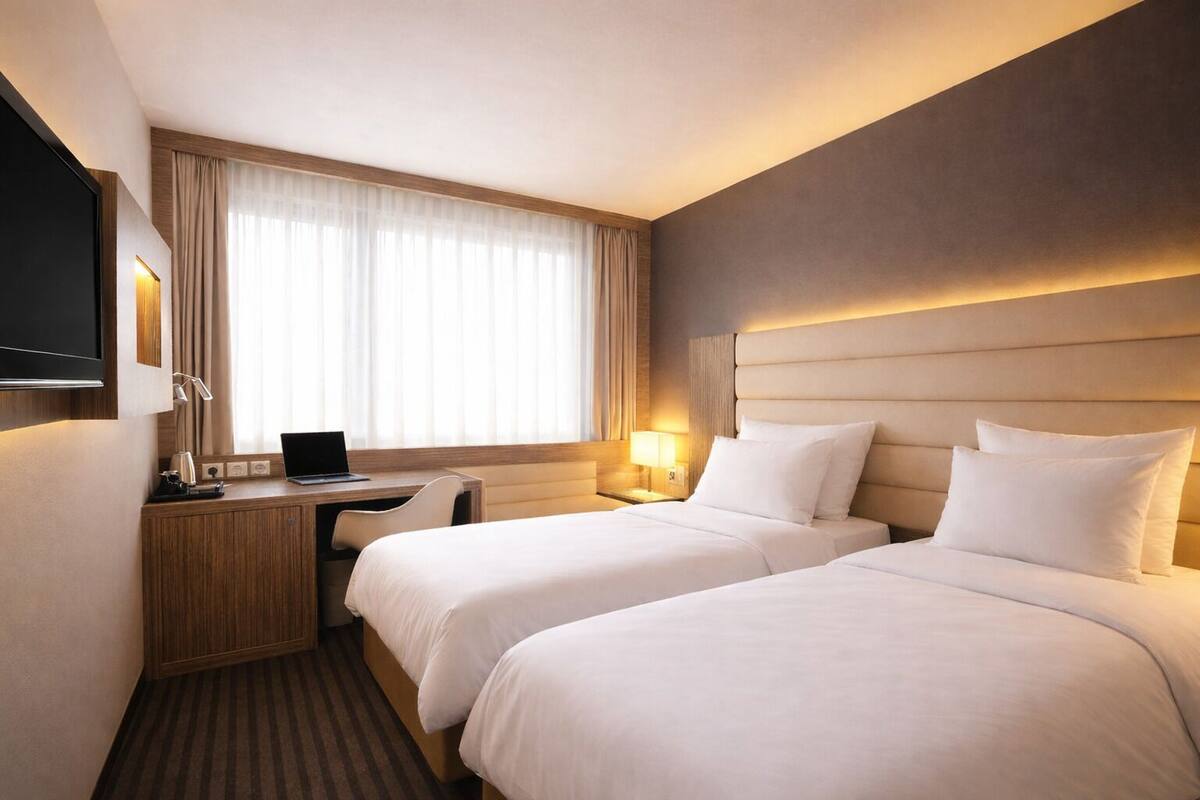 A hotel room with two beds, a desk, a TV, and a window with curtains.