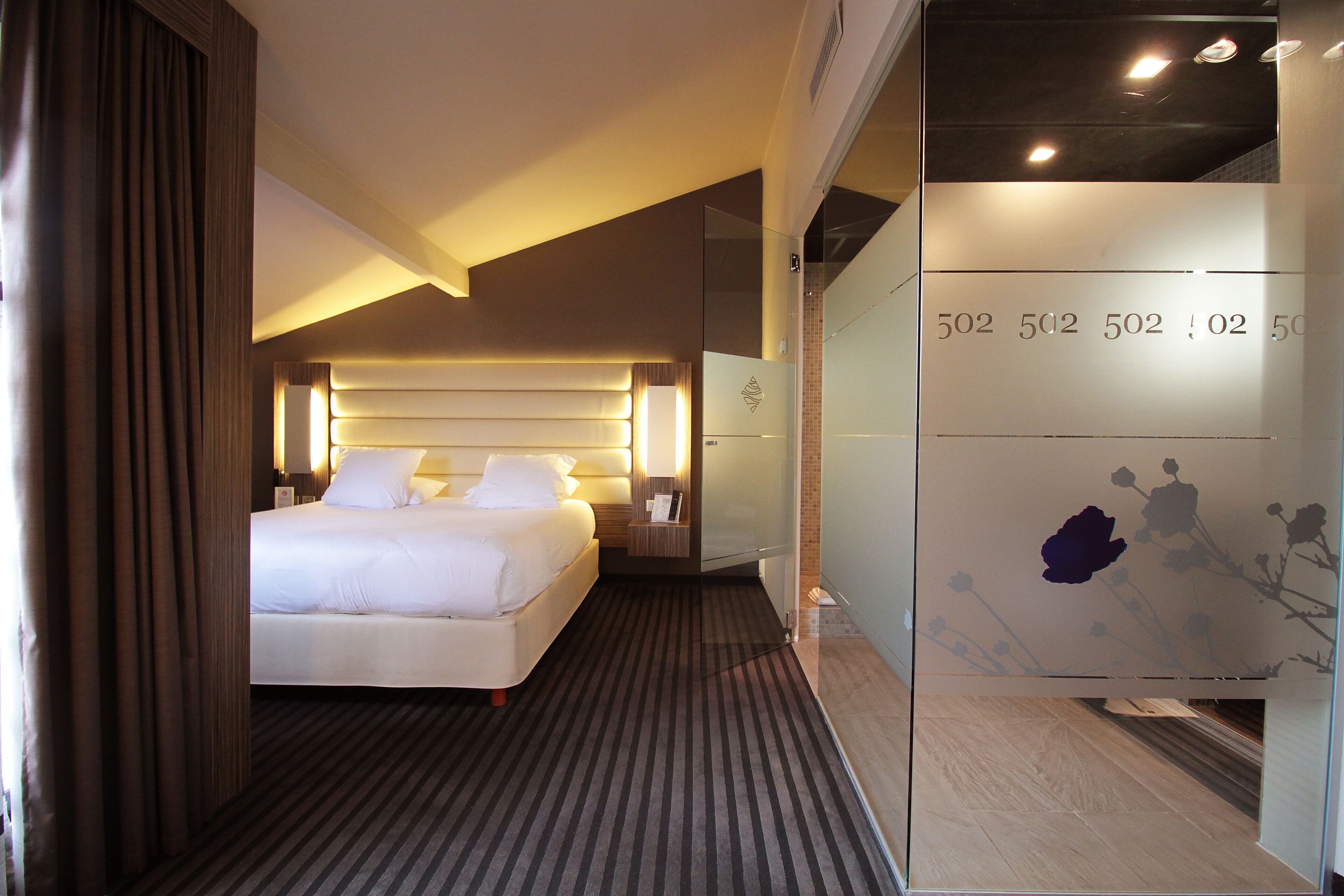 Ein Hotelzimmer mit einem großen Bett, einem Nachttisch, einer Wandlampe und einer Trennwand mit floralem Muster.
