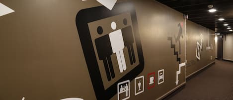 A corridor with directional arrows and icons indicating facilities such as restrooms, a staircase, and a meeting area.