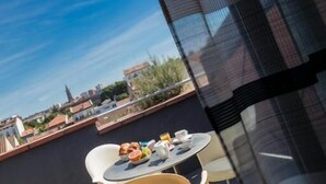 Un balcón con una mesa dispuesta para dos personas, con vista a un paisaje urbano.