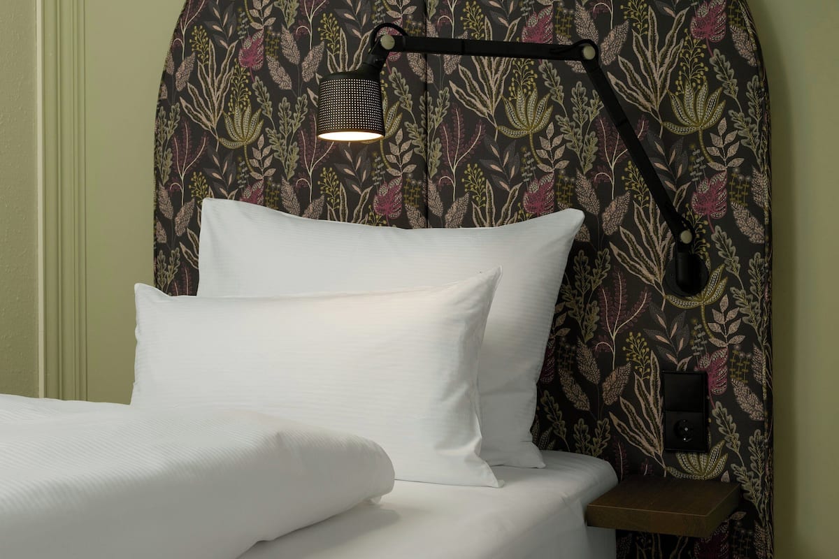 A neatly made bed with white linens, a bedside table, and a wall-mounted lamp.