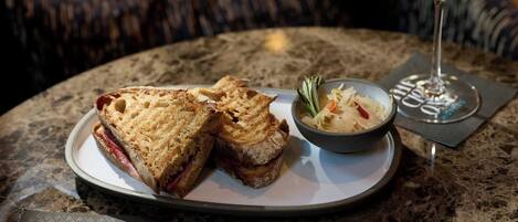 A sandwich and a bowl of soup on a table with a wine glass.