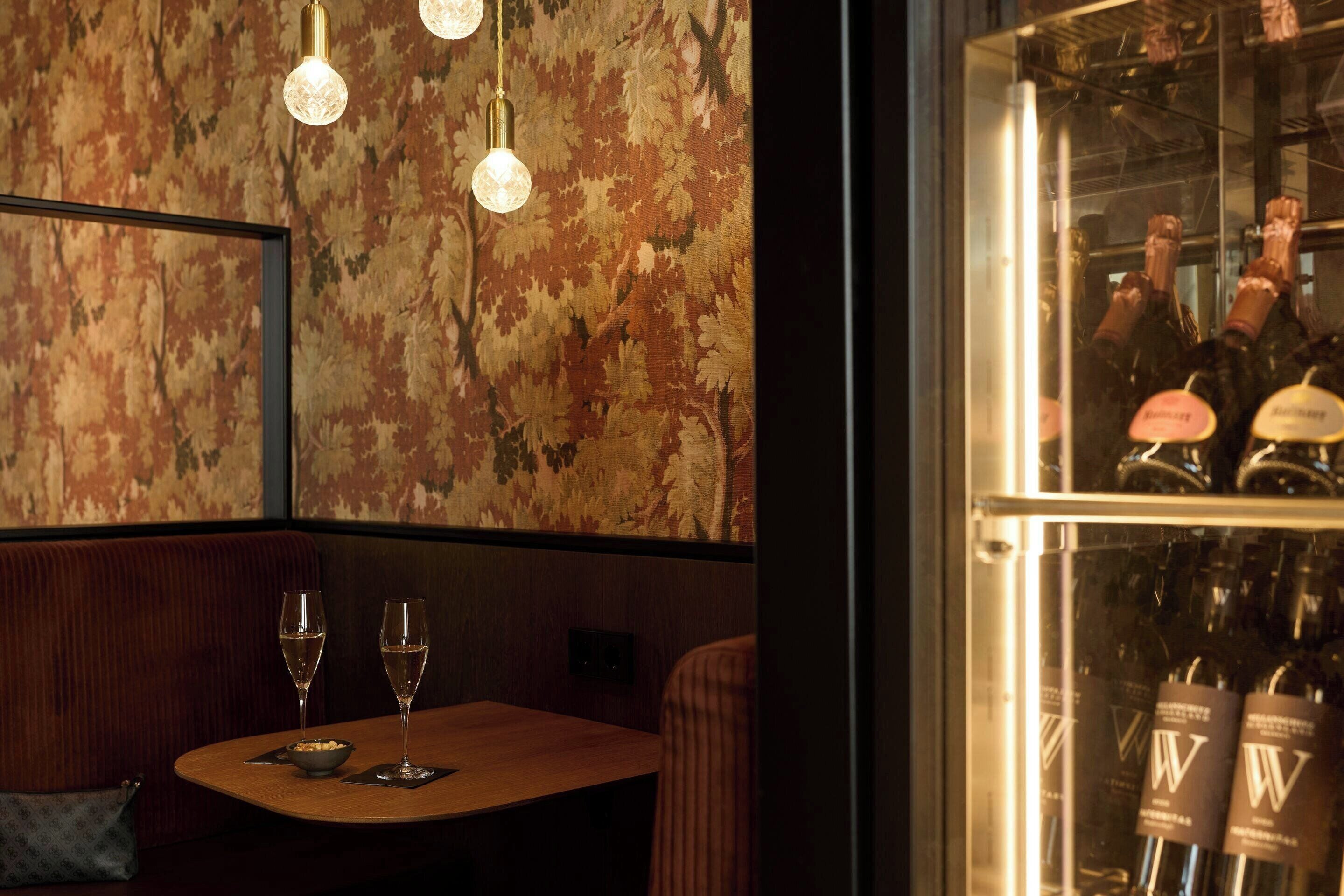 Un interno ristorante con un tavolo in legno, due bicchieri da vino, una ciotola di frutta secca e un muro decorato.