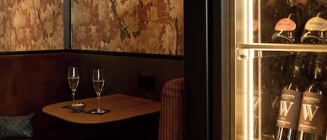 A restaurant interior with a wooden table, two wine glasses, a bowl of nuts, and a patterned wall.