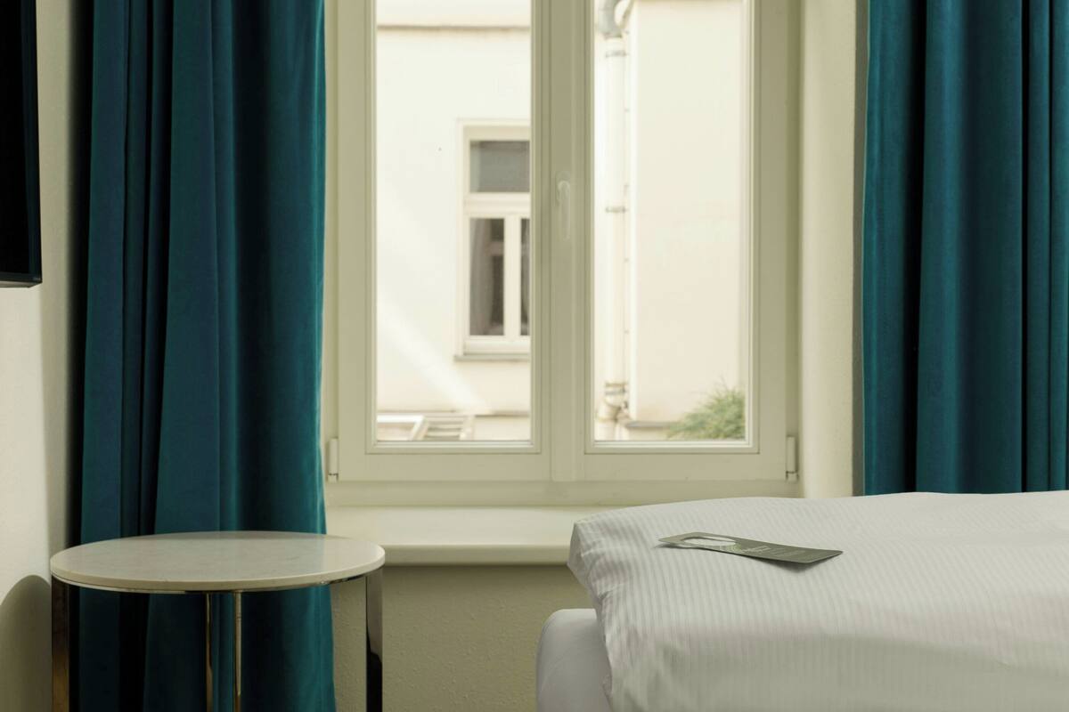 Una habitación de hotel con una cama, una mesa redonda y un ventanal con cortinas.
