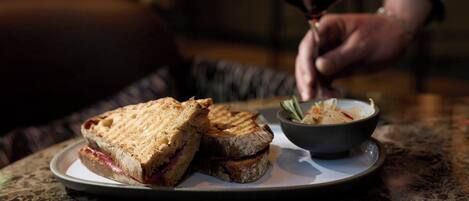 Un sándwich en un plato con un tazón de ensalada y una copa de vino tinto.