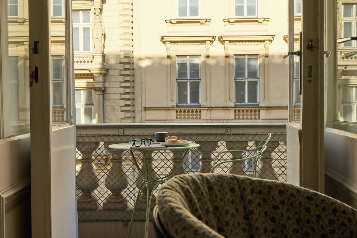 A balcony with a chair, a table, and a view of a building with classical architecture.