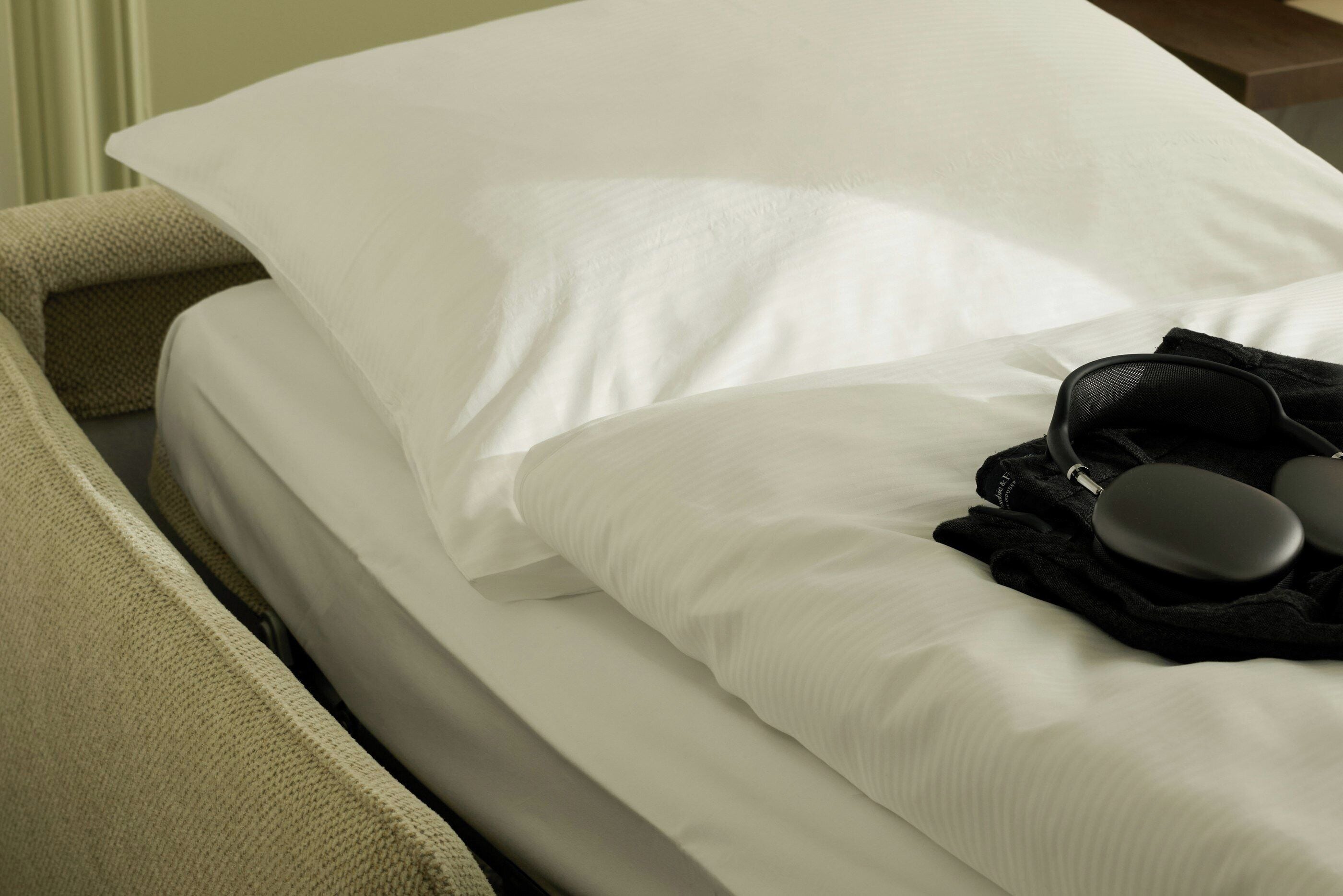 Una cama con ropa blanca y una almohada negra.