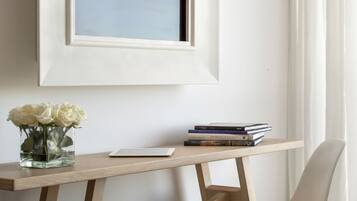 A minimalist room with a desk, a chair, a framed picture, a vase with flowers, and a tray with a cup, teapot, and cookies.