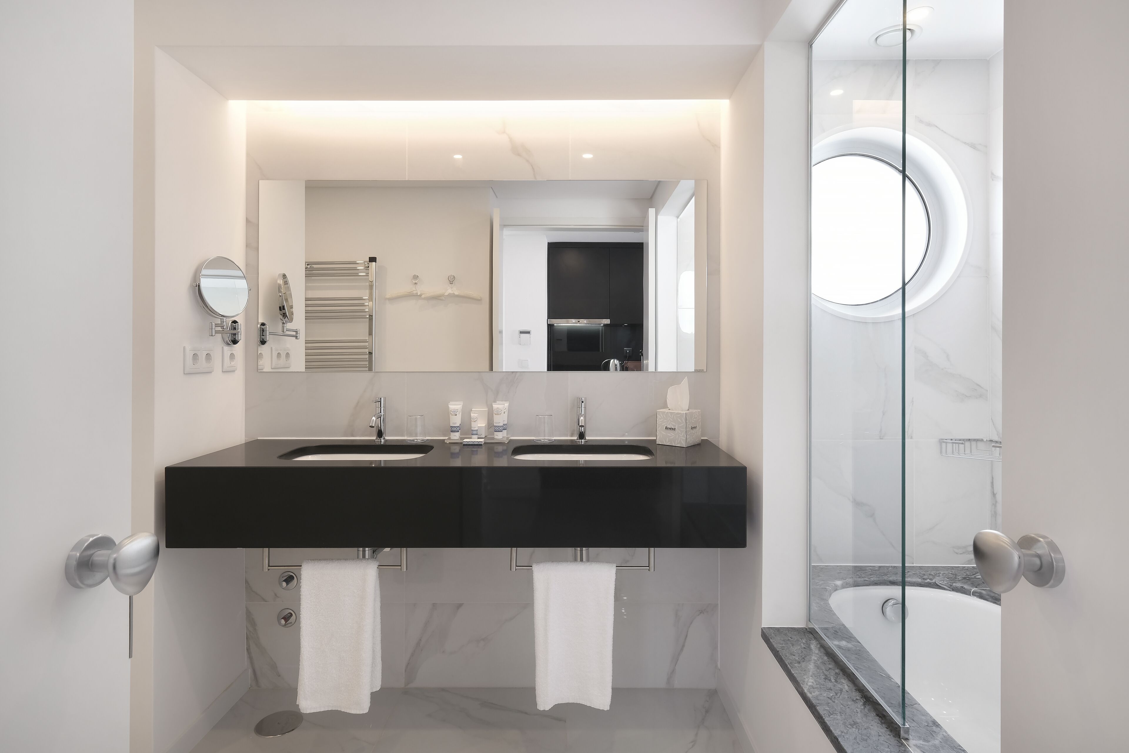 A modern bathroom with two sinks, a large mirror, and a glass-enclosed shower.