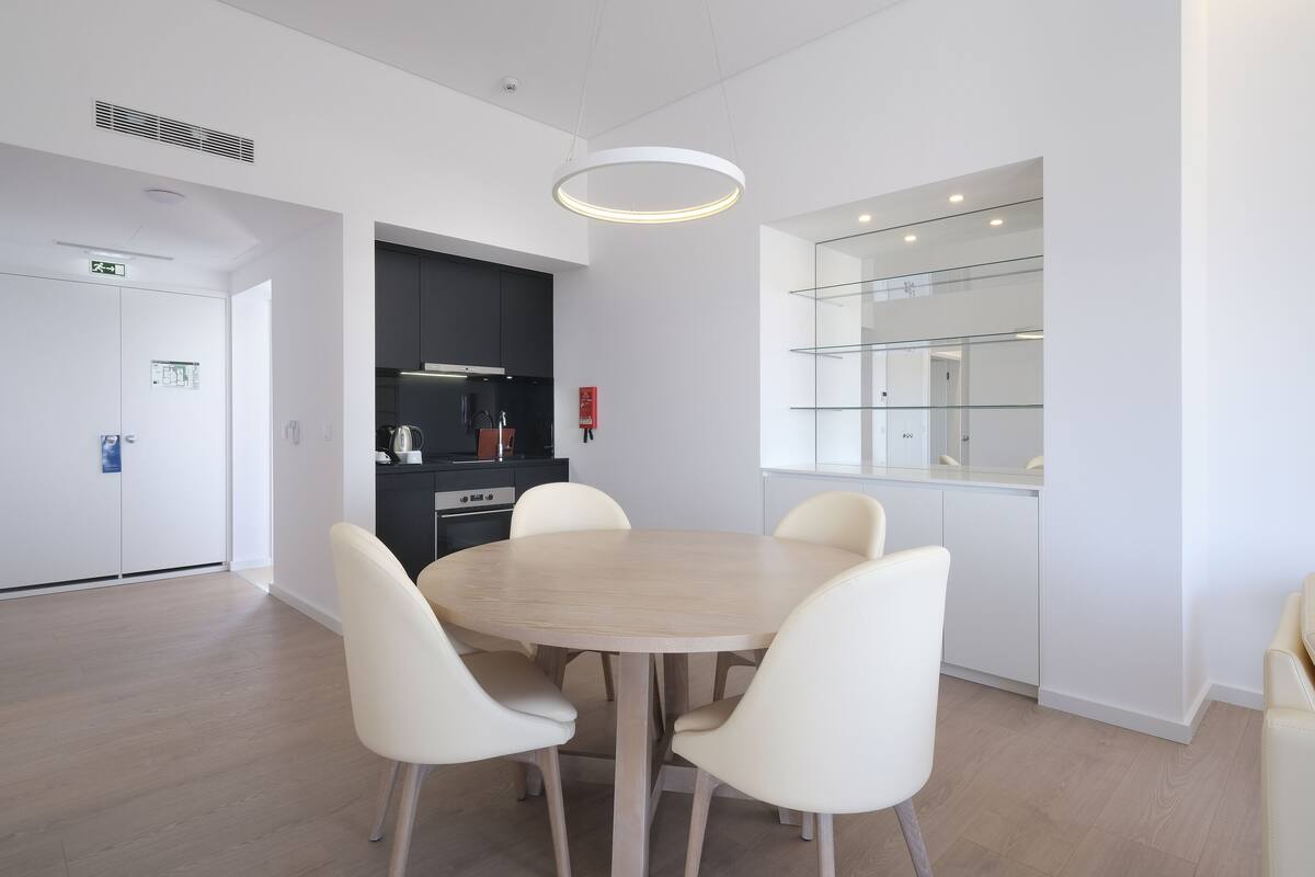 A modern kitchen with white cabinets, a round wooden table, and four white chairs.