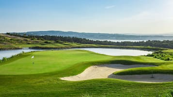 Un parcours de golf avec un plan d’eau, des bunkers de sable et un drapeau sur le green.