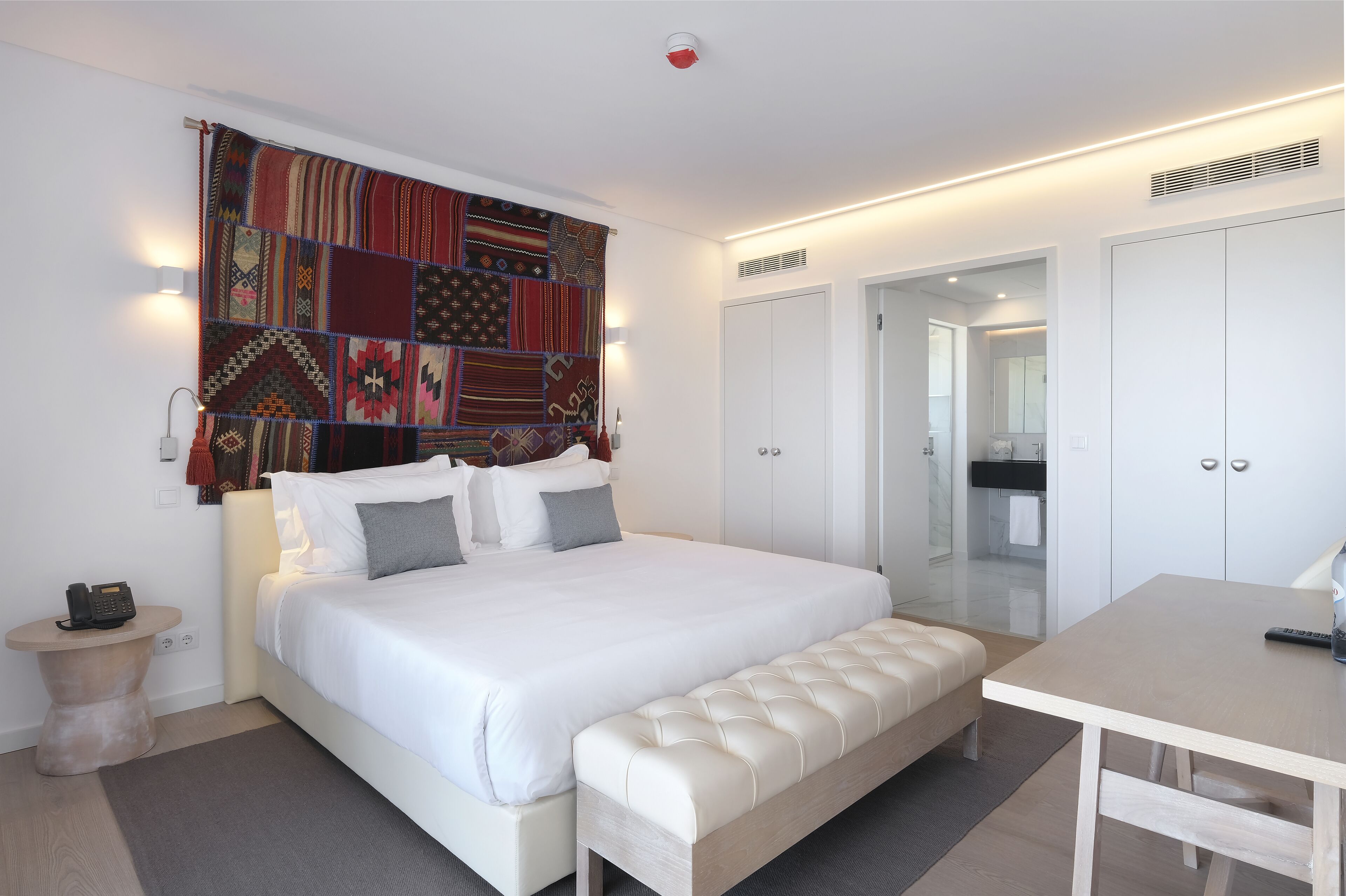A modern bedroom with a large bed, a bedside table, a bench, and a small table.